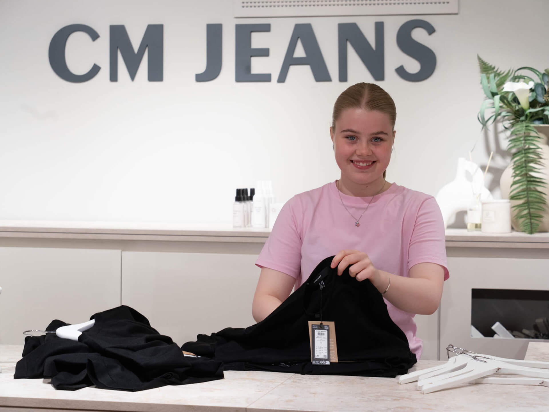 Ansatt bretter klær bak disken hos CM Jeans